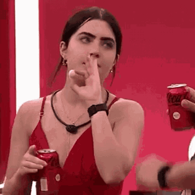 a woman in a red dress is holding a can of coca cola and covering her mouth .