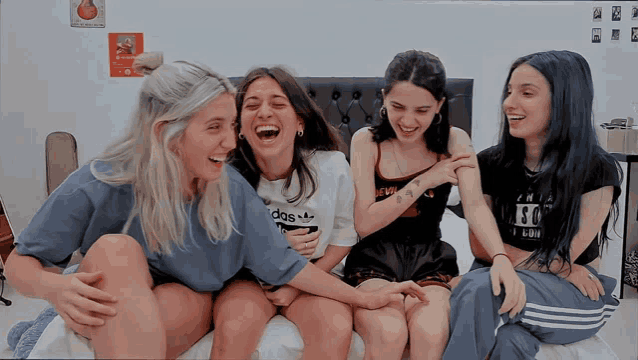 four girls are sitting on a bed with one wearing a shirt that says adidas