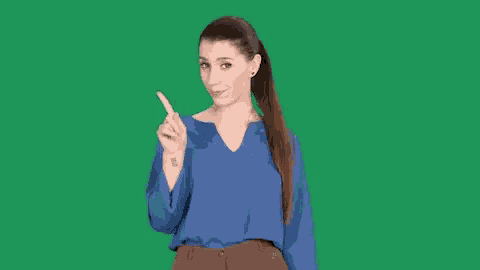 a woman in a blue shirt and brown pants is pointing her finger up .