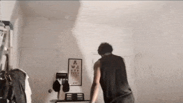 a man in a black tank top is standing in a room with a poster on the wall that says a wi eye chart