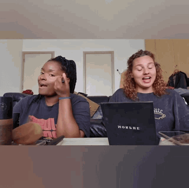 two women are sitting at a table with a laptop that says ' mockbe ' on it