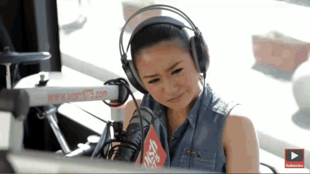 a woman wearing headphones is sitting in front of a microphone with a sign on it that says ' subscribe '