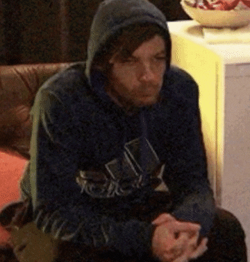 a man in a hoodie is sitting on a couch with his hands folded .