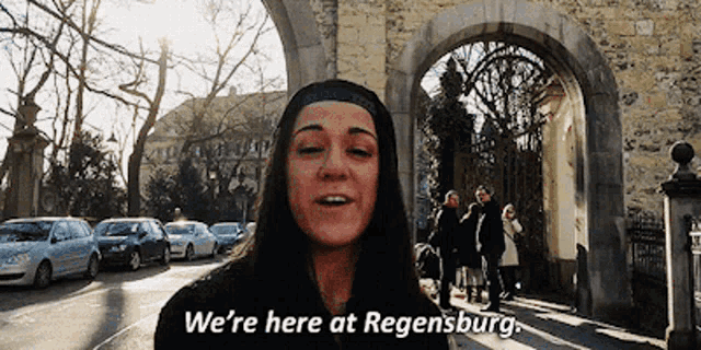 a woman says " we 're here at regensburg " while standing in front of a stone archway