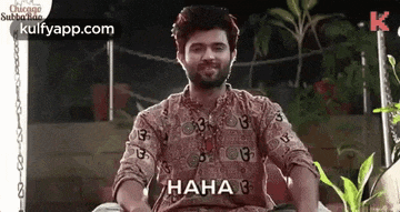 a man in a floral shirt is sitting on a swing and laughing .