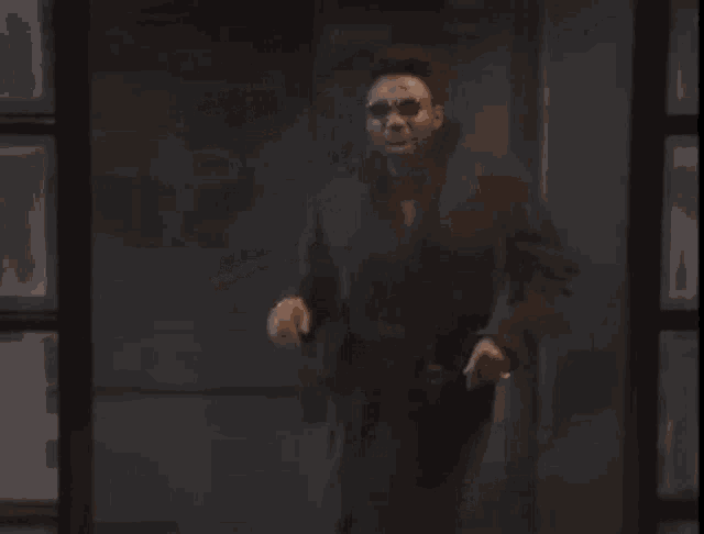 a man wearing sunglasses and a suit is walking through a doorway .