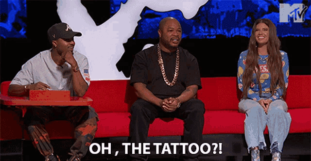 a group of people are sitting on a red couch and one of them is saying oh the tattoo
