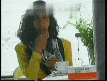 a woman in a yellow jacket is sitting at a table with a cup of coffee and a box of aspirec acid .