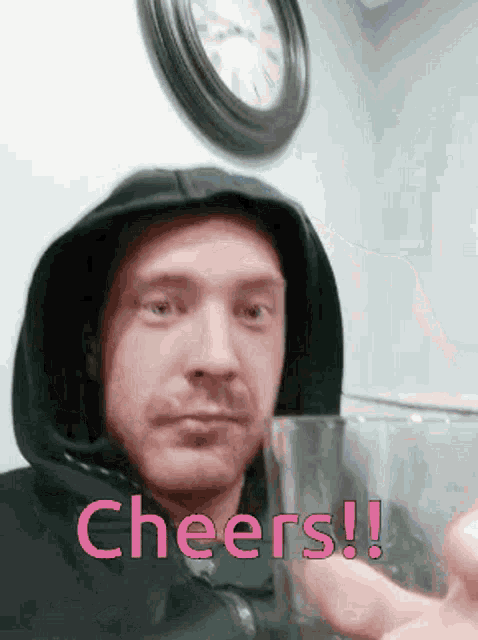 a man wearing a hoodie is holding a glass with the words cheers written on it .
