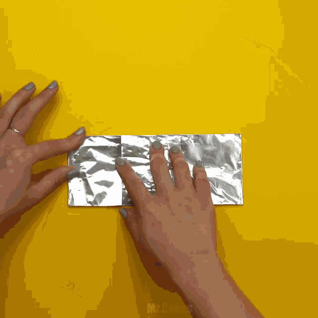 a person is holding a piece of aluminum foil on a yellow background with the words mr.cakes below them