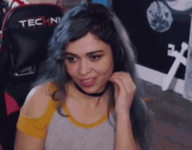 a woman with blue hair is sitting in a chair with a choker on her neck .