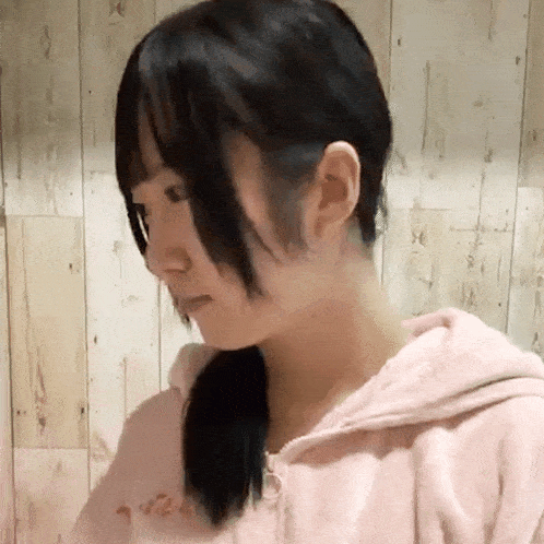 a close up of a woman wearing a pink hoodie against a wooden wall .