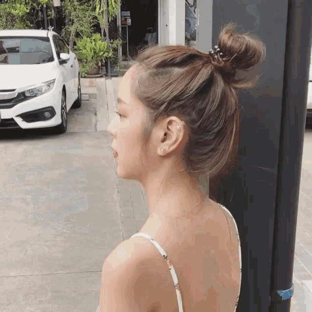 a woman with her hair in a bun stands in front of a white honda