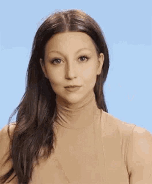 a woman is wearing a tan turtleneck and making a face .