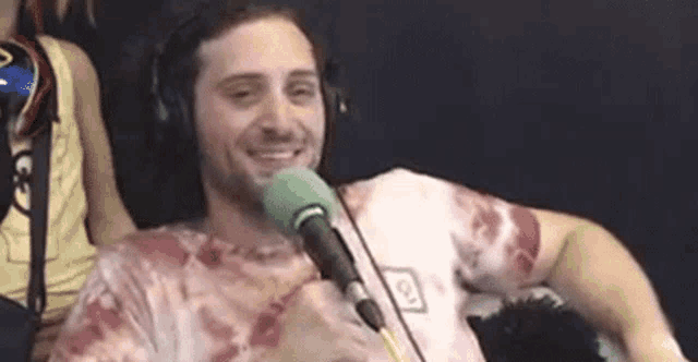 a man wearing headphones and a tie dye shirt is sitting in front of a microphone .