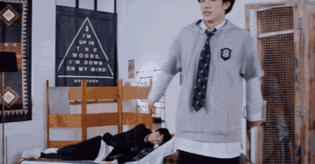 a man in a tie is standing next to a man laying on a bed