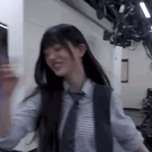 a woman in a striped shirt and tie is standing in a room with a camera .