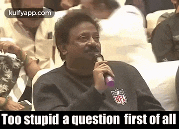 a man is sitting in a stadium holding a microphone and talking into it .