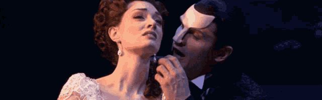 a man with a mask on his face talks to a woman in a white dress