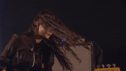 a woman with long hair is playing a bass guitar on stage .