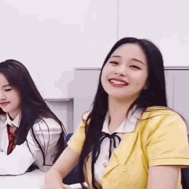 a girl in a yellow jacket is smiling while sitting next to another girl in a white shirt .