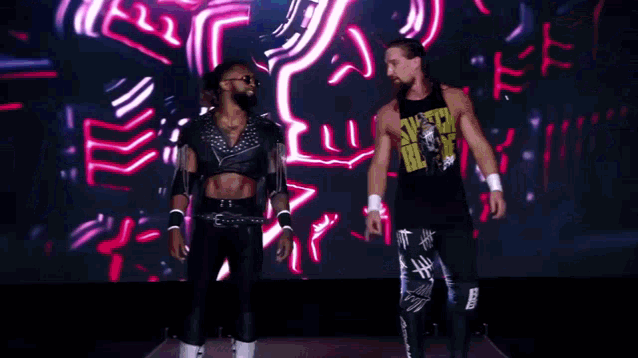 two men are standing next to each other in front of a large screen .
