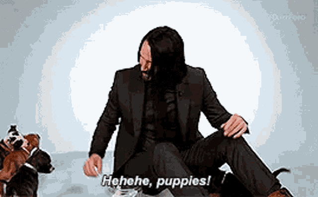 a man in a suit is sitting on the floor surrounded by puppies and talking to them .