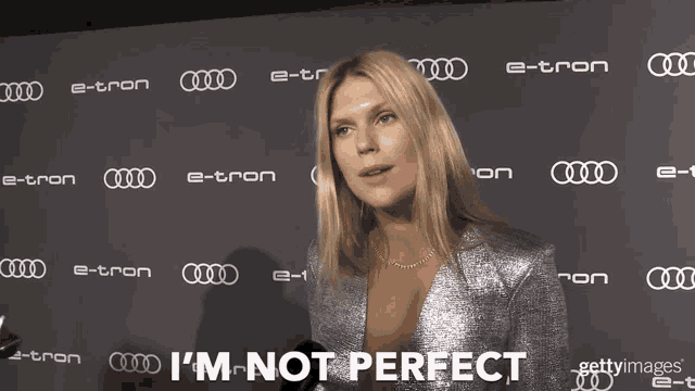a woman says i 'm not perfect in front of a wall of e-tron logos