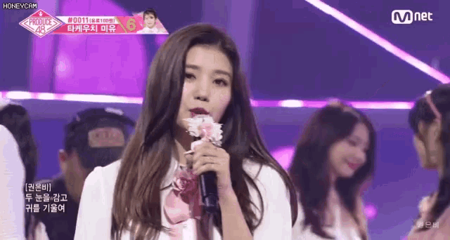 a girl is holding a flower in front of a microphone while another girl looks on .