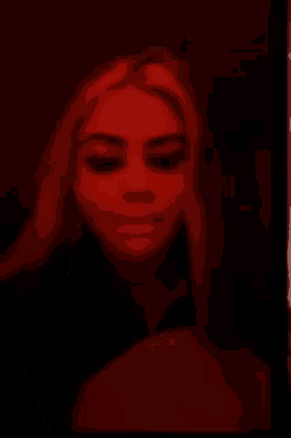 a woman is covering her face with her hand in a dark room with red lights .