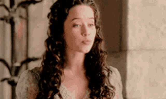 a woman with long curly hair is wearing a white dress and standing next to a wall .