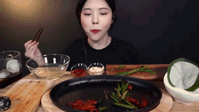 a woman is eating a plate of food with chopsticks and a bowl of sauce on a table