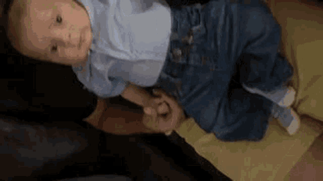 a baby is laying on a bed holding a person 's hand .