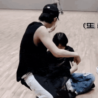 a man in a black tank top sits on a wooden floor