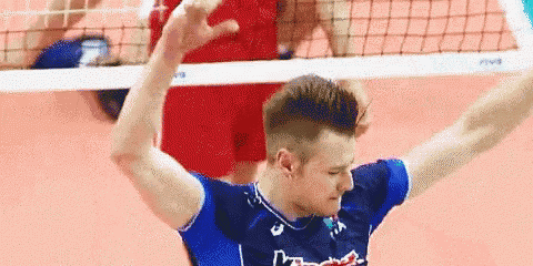 a man in a blue shirt is playing volleyball on a court with his arms outstretched .