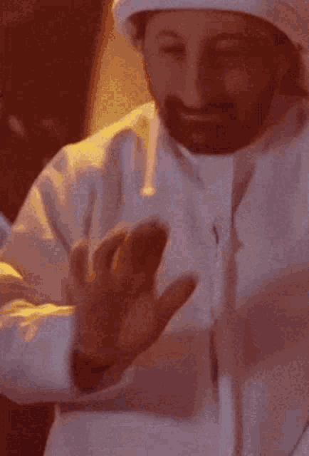 a man with a beard wearing a white head scarf is covering his nose with his hand
