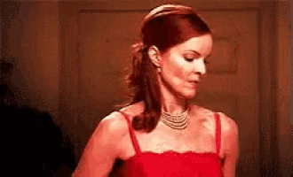 a woman in a red dress and pearls is standing in a room .