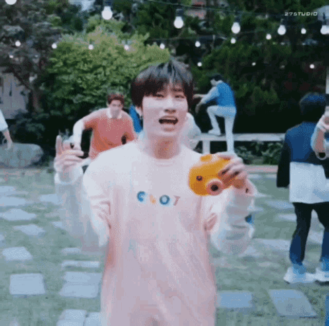 a young man in a pink shirt is holding a yellow toy camera in his hand .