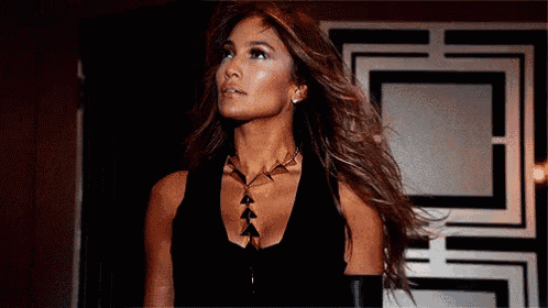 a woman in a black tank top and necklace is standing in front of a door .