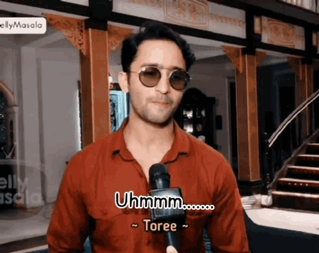 a man wearing sunglasses and a red shirt is talking into a microphone and says uhhmm toree