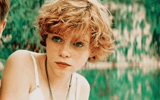 a young girl with short curly hair is wearing a white tank top