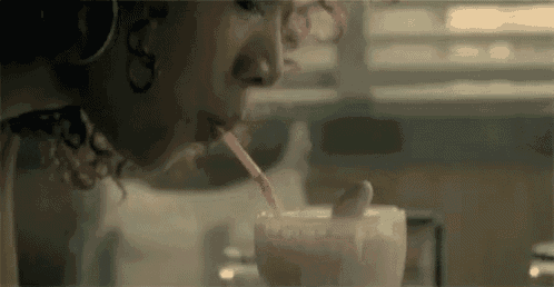 a woman is drinking a milkshake through a straw at a diner .