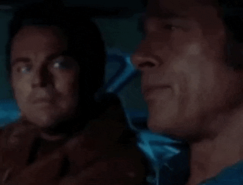 a man in a leather jacket is talking to another man in a car and the man is saying holy shib .