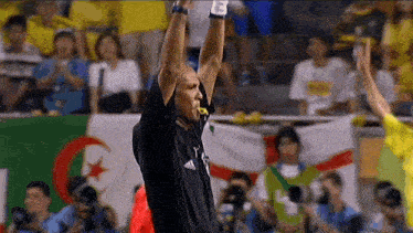 a referee wearing a black adidas shirt holds up his arms in the air