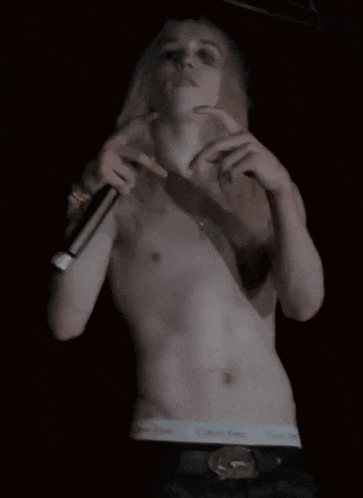 a man without a shirt is holding a microphone in front of his chest