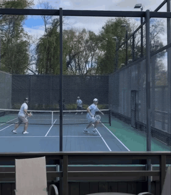 two men are playing tennis on a tennis court behind a fence