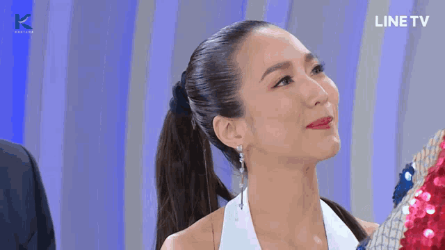 a woman with a ponytail looks at the camera with a line tv logo in the background