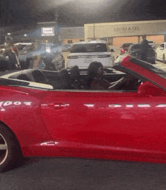 a woman is sitting in a red sports car in front of a lyndi & co. store
