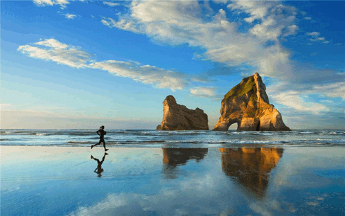 a person is running on a beach near a large rock