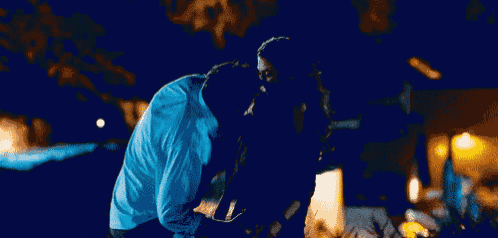 a man in a blue shirt is hugging a woman in a dark room .